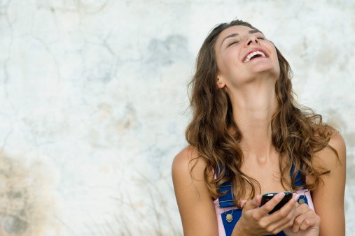 Young woman holding cell phone, laughing